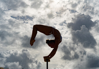Flexible female circus Artist keep balance on hands against amazing cloudscape. Individuality,...
