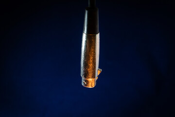 Closeup of Dangling Worn out and Scratched Male XLR Connector isolated on Blue Background with Orange Lighting