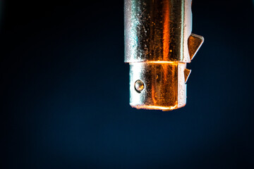 Macro Closeup of Worn out and Scratched Male XLR Connector Isolated on Blue Background with Orange Lighting