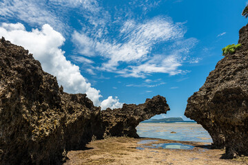 Coral platform between coastal rocks at low tide, small sea pool, blue sky with white cirrus clouds. Iriomote Island.