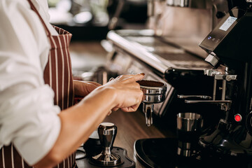 Close up view of barista prepare brewing coffee powder in portafilter with grinder machine in the cafe.