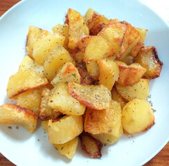 Roast potatoes seasoned with sea salt and mixed herbs on a white dish.
