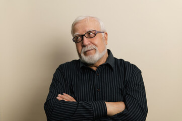 Obraz premium elderly man in glasses and black shirt folded hands on chest, waist portrait, light background, studio