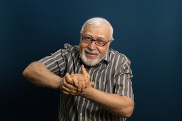 elderly gray-haired man in glasses and a black shirt, grandfather, rubs his hands with pleasure, emotions in the frame, waist portrait, blue background, studio