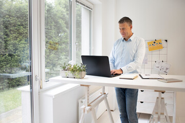 handsome businessman with blue shirt works at high table and is writing something on his black laptop