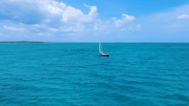 Traditional dhow boat sailing on pristine tropical sea, Zanzibar. Aerial forward