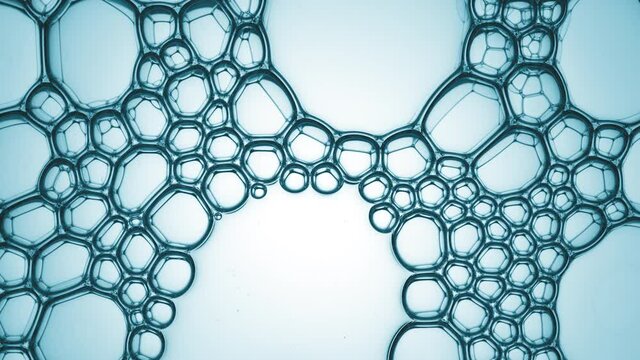 A lot of clear different sized bubbles burst spontaneously at a time against cyan background | Macro shot of moisturizer with hyaluronic acid for its commercial
