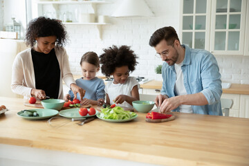 Loving young multiracial family with diverse small daughters cook healthy vegetarian salad for dinner lunch in kitchen. Caring multiethnic mom and dad prepare food with children. Adoption concept. - Powered by Adobe