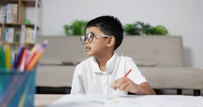 Asian boy glasses bored while drawing in living room at home