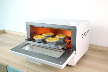 white modern design toaster oven with egg tart inside is on the wooden table with white cement wall...