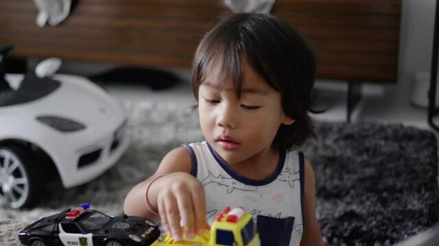Asian boy playing with his police car and toy truck and is distracted.