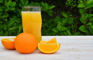refreshing fruit summer cocktail or juice in a glass glass, cooling orange drink with a slice of pineapple outdoors on wooden table on green leaves background, eco friendly and organic concept
