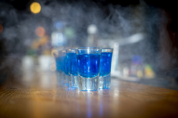 Selective focus shot of blue drink in shot glasses with dry ice smoke effect on a wooden bar counter