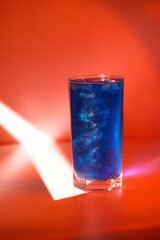 Closeup vertical image of blue cocktail with shimmer shining at red minimal background with spotlight
