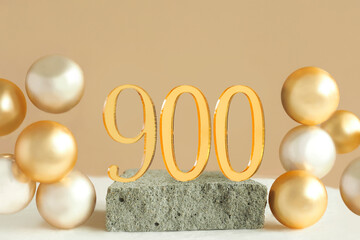 Number 900 on a concrete podium and volumetric golden balls on a beige background. Copy space..
