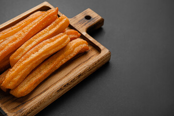 Board with tasty churros on dark background, closeup