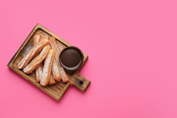 Board with tasty churros and melted chocolate sauce on color background