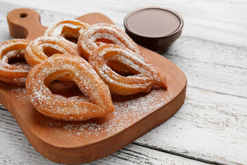 Board with tasty churros and melted chocolate sauce on light wooden background, closeup