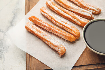 Board with tasty churros and melted chocolate sauce on light background, closeup