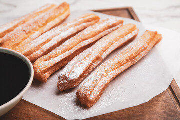 Board with tasty churros and melted chocolate sauce on light background, closeup
