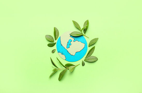 Paper planet Earth with green leaves on color background. Ecology concept