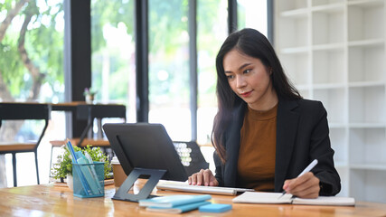 Fototapeta premium Beautiful businesswoman making note on notebook during watching webinar on computer laptop.