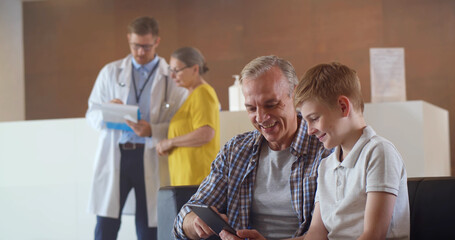 Obraz premium Father and son using digital tablet sitting in hospital waiting room