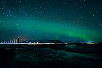 night photography of a landscape of a bridge over a river with cars crossing and with an aurora borealis on top