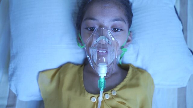 Close up top view of young kid breathing on ventilator oxygen mask due to coronavirus covid-19 breathlessness or dyspnea - concept of children Healthcare and medical during third wave pandemic.
