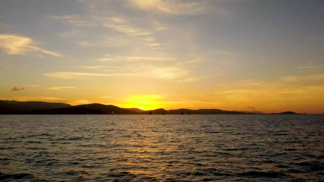 Taken from another boat  A mumber of racing Sail boats can be seen silhouetted against a colorful skyline by the sunset off the coast of Airlie Beach in North Queensland Australia.
