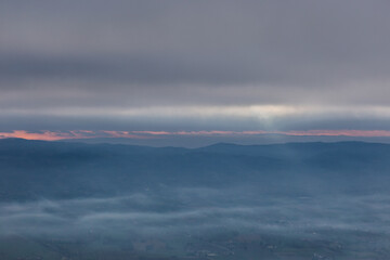 Fototapeta na wymiar View from above of sunrays coming down on mist between hills and mountains in Umbria valley, Italy