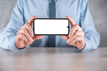 Businessman in a blue shirt at workplace at the table holding a mobile phone, smartphone with a white screen. Screen facing the camera. Mock up.Concept of technology, connection, communication.