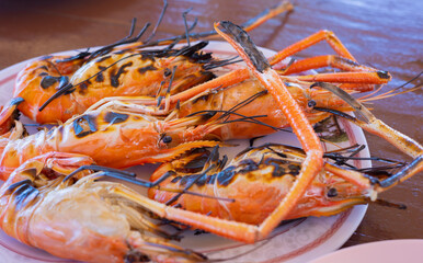 Close up and selective focus shot of many large grilled shrimps with orange color of well cooking served in plate as seafood for delicious and tasty meal and healthy in restaurant.
