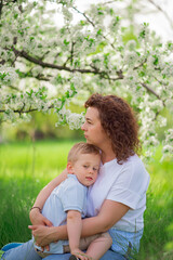 Naklejka na ściany i meble mother sit, holds young son in flowering spring garden. parental love and care