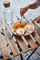woman hands with fork and knife eating schnitzel with egg, potatoes and cabbage on the terrace of a local diner on the street