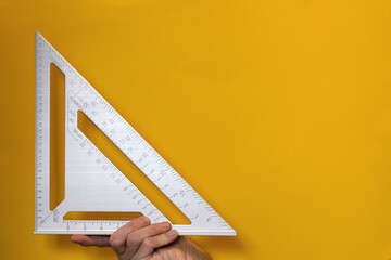 Close-up of professional steel ruler in triangular shape in hand on yellow background. Drawing tool or architect measures distance. Finger length size, 90 degree right angle, or hill image association - obrazy, fototapety, plakaty