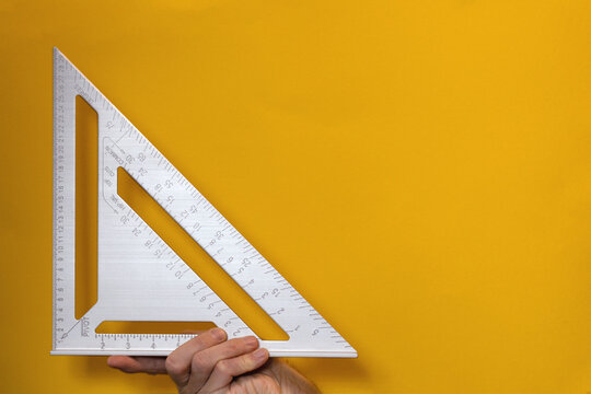 Close-up of professional steel ruler in triangular shape in hand on yellow background. Drawing tool or architect measures distance. Finger length size, 90 degree right angle, or hill image association