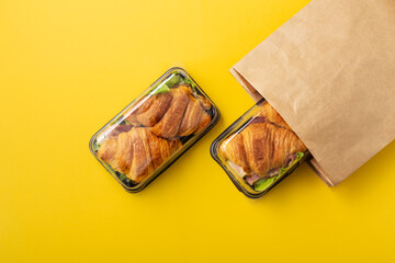 Croissant sandwich in takeout food container and paper bag