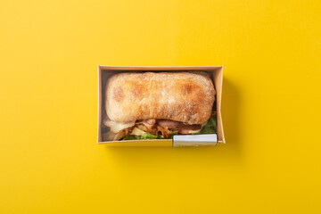 Ciabatta sandwich in takeout food container on yellow background