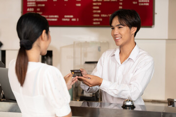male receptionist or hotel front desk smiling and receiving credit card from woman guest