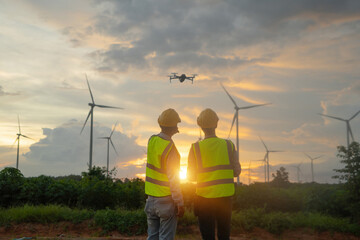 Teamwork of Asian windmill engineer group, worker working, control a drone on site at wind turbines...