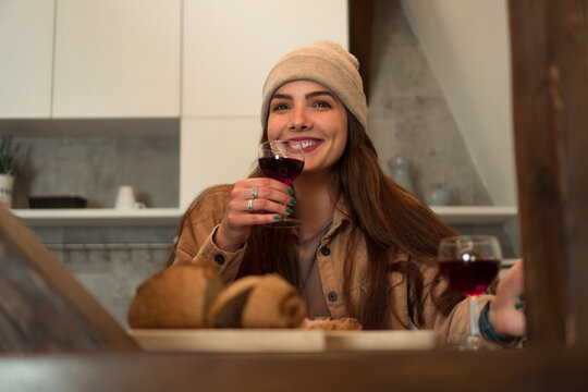 A beautiful young woman smiles and feels happy while having dinner and a glass of red wine with a person not shown in a photo.