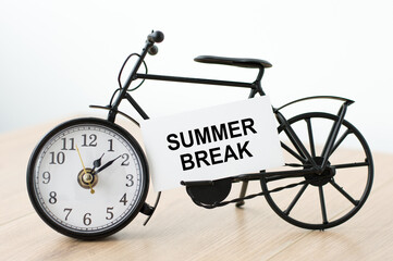 Text Summer Break on a white card that lies on the clock in the shape of a bicycle on the table