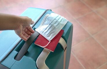 International travel during pandemic. Hand carrying luggage bag with face mask and passport.