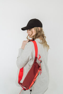 a blonde woman wearing a cap on her head with a small red sports bag on a white background. a woman in sportswear. the concept of accessories and hats