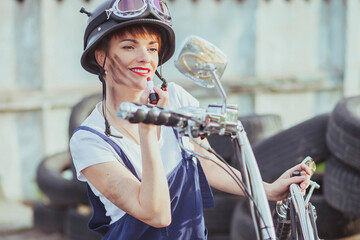 Girl auto mechanic in a helmet looks in a motorcycle mirror and paints lips
