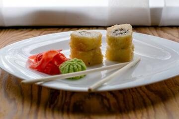 baked sushi stacked on top of each other in two piles with eel wasabi ginger and chopsticks on a white plate