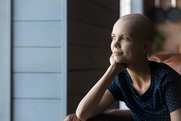 Fototapeta na wymiar Thoughtful hairless ill woman fighting against cancer, looking away at window with hope, thinking of life after treatment and chemotherapy, dreaming of recovery. Oncology patient, disease concept