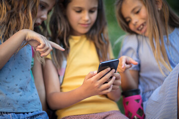 Fototapeta premium Three little girls using smart phone in nature. Focus on hands.