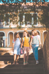  School girls going to home after school. Three little school girls walking and holding hands.